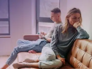 Mulher chateada sentada no sofá de costa para o marido chateado também sentado no mesmo sofá!