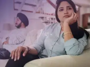 Homem sentado em uma extremidade do sofá com semblante sério e desconfortado enquanto a mulher está sentada na outra extremidade do sofá com semblantes preocupado e triste, provavelmente um casal em crise!