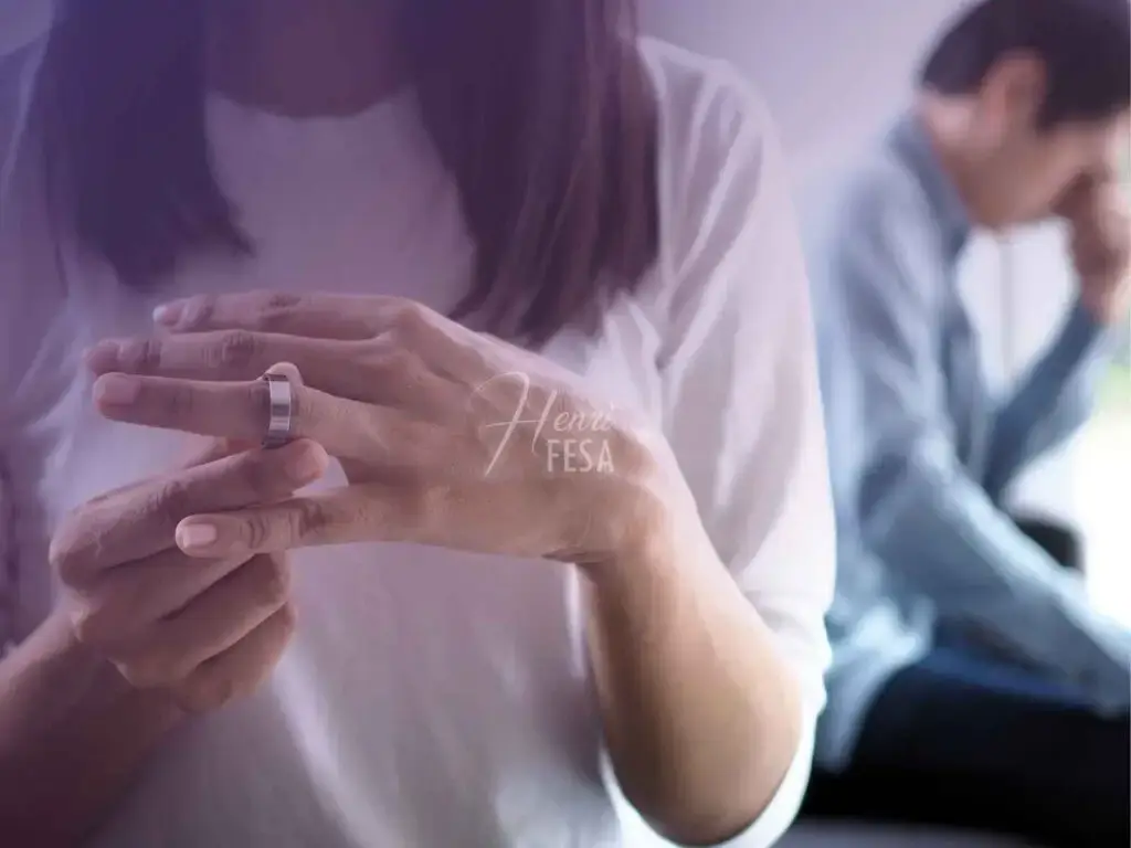 Mulher partindo e tirando a aliança de casamento do dedo anelar da mão esquerda enquanto o homem está desolado logo ao fundo da imagem, sentado com a mão no rosto!