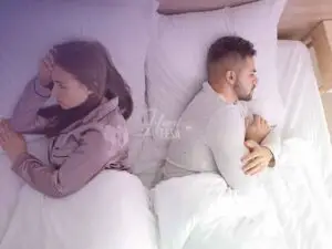 Homem em mulher deitados na cama, um de costas para o outro, ambos com expressão reflexiva, dando a entender que é uma crise na relação!