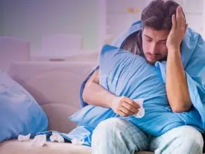 Homem sentando no sofá com a mão na cabeça indicando que está com dor e vários lenços já usados espalhados pelo sofá!