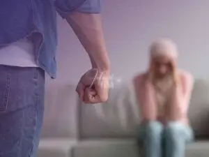 Homem de mãos fechada, mulher sentada no sofá com as mãos tapando os ouvidos, com olhos fechados com expressão de medo!