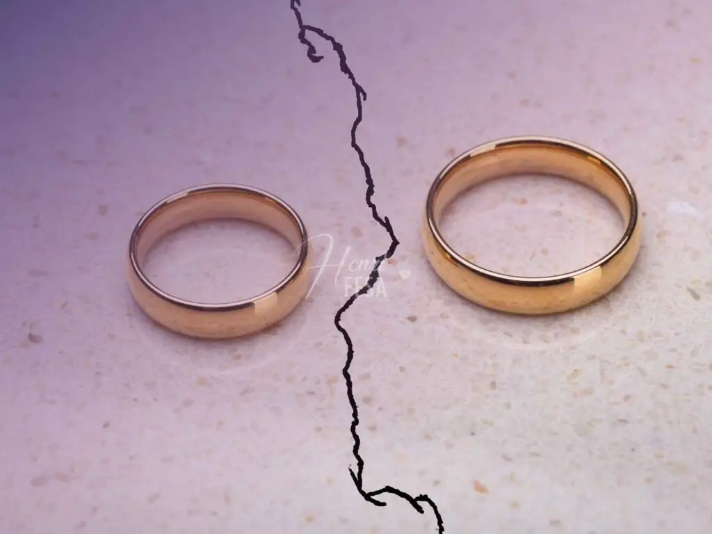 Duas alianças douradas, uma maior e outra menor, ambas sobre em uma superfície lisa, cada uma de um lado de uma rachadura nesta superfície, simbolizando um casamento rachado!