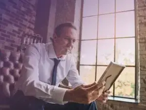 Homem de meia-idade sentado em uma poltrona, segurando um porta-retratos e olhando para a foto enquanto relembra coisas importantes!