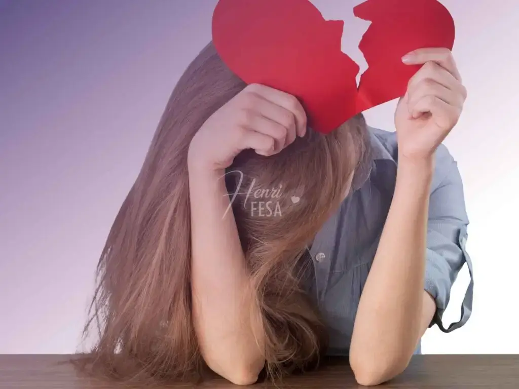 Mulher debruçada sobre uma bancada, segurando um coração de papel que está partido ao meio!