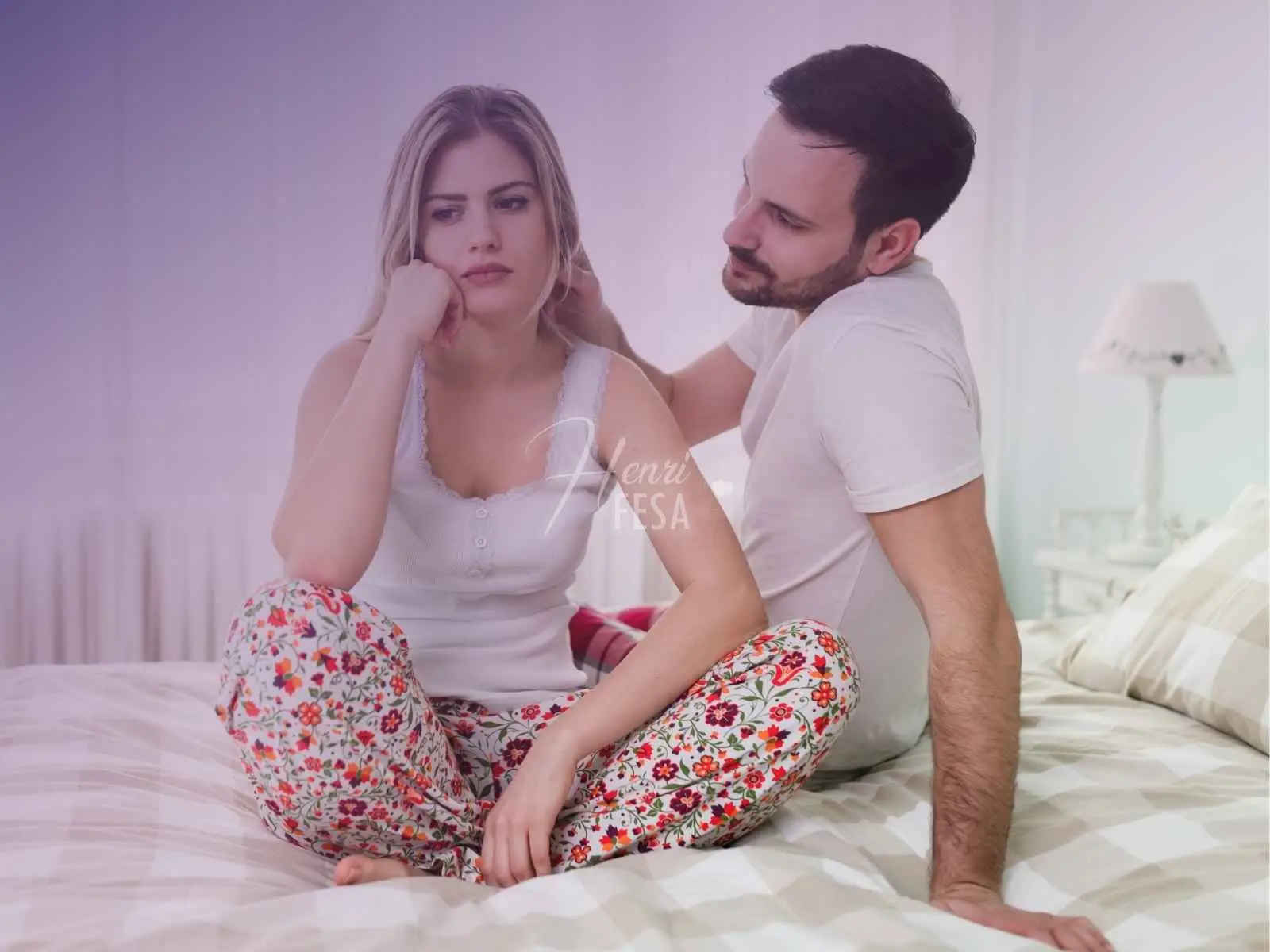 Mulher sentada à cama, com expressão de preocupação, homem a consolando