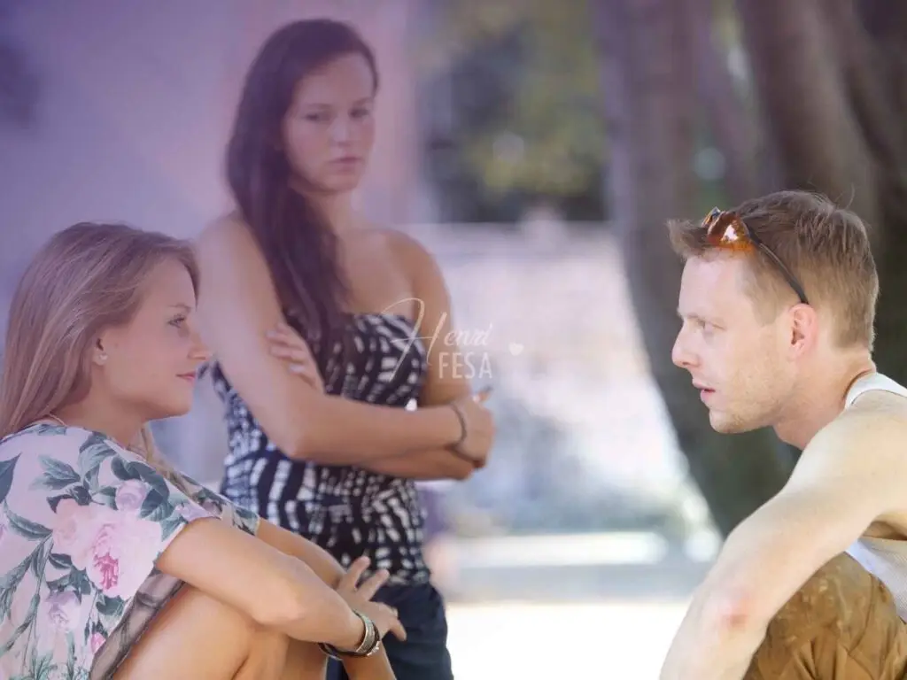 Homem conversando com mulher, enquanto outra mulher mais ao fundo da imagem está observando com olhar irado de ciúmes!