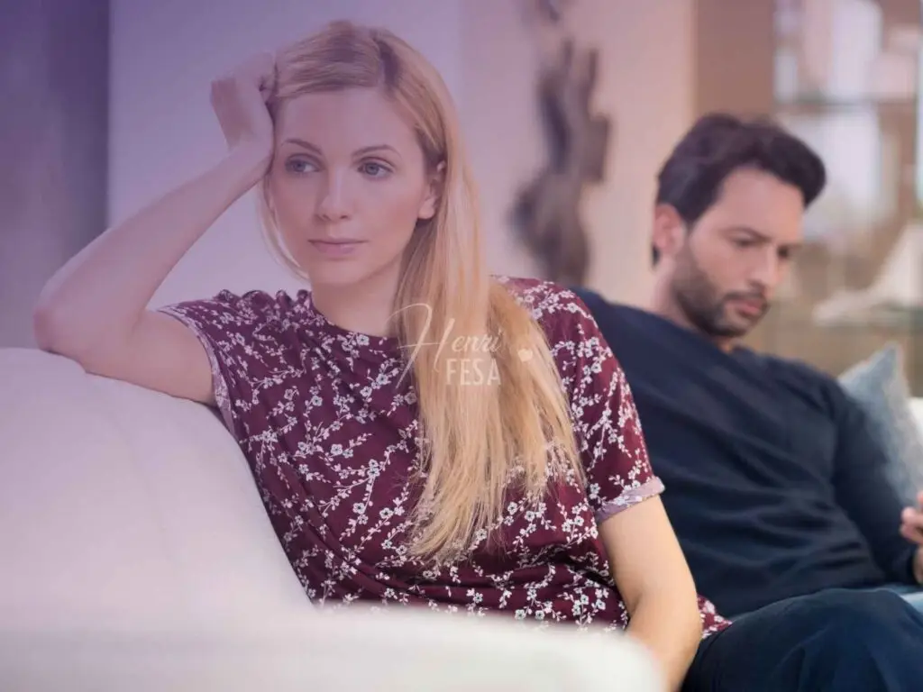 Casal homem e mulher, mulher sentada de costas no sofá com semblante de descontente, marido sentado no mesmo sofá sem se importar, mexendo no celular!