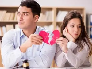 Homem e mulher, sentados um ao lado do outro de rosto virado, ambos segurando a metade de um coração partido simbolizando decepção amorosa!