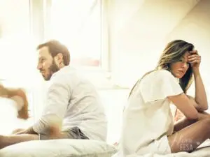 Casal homem e mulher sentados na cama um de costas para o outro, ambos com semblante de descontadamente por relacionamento conturbado!