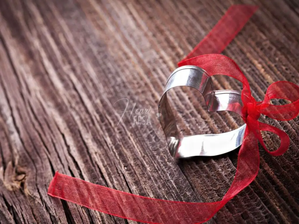 Amarração Amorosa com Oxum, Pomba‑gira e Maria Padilha Um coração de metal com um laço vermelho amarrado, simbolizando a Amarração Amorosa com Oxum!