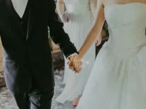 Casal homem e mulher de mãos dadas no dia de seu casamento, ela de vestido de noiva e ele a caráter, passando a imagem de um casamento blindado!