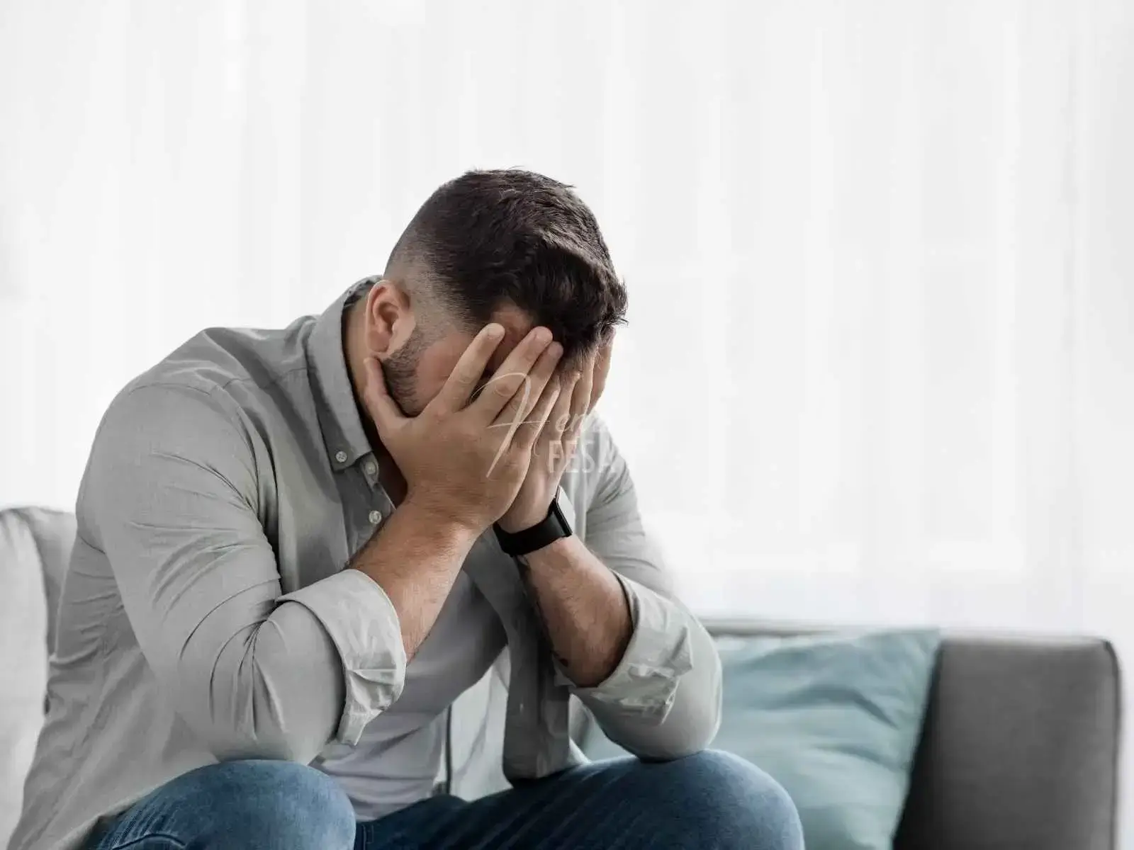 Um homem sentado ao sofá com as mãos no rosto, triste, revelando que homens que se separaram sofrem calados!