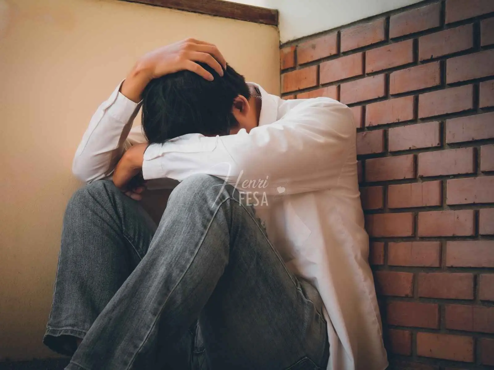 Homem sentado no chão, encostado na parede, com a cabeça entre as pernas e as mãos na cabeça, um dos sinais de um homem infeliz no casamento mais evidentes!