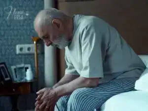 Homem 50+ sentado à beira da cama, cabisbaixo, com pensamentos negativos e tristezas, um dos motivos para o marido negativo existir!