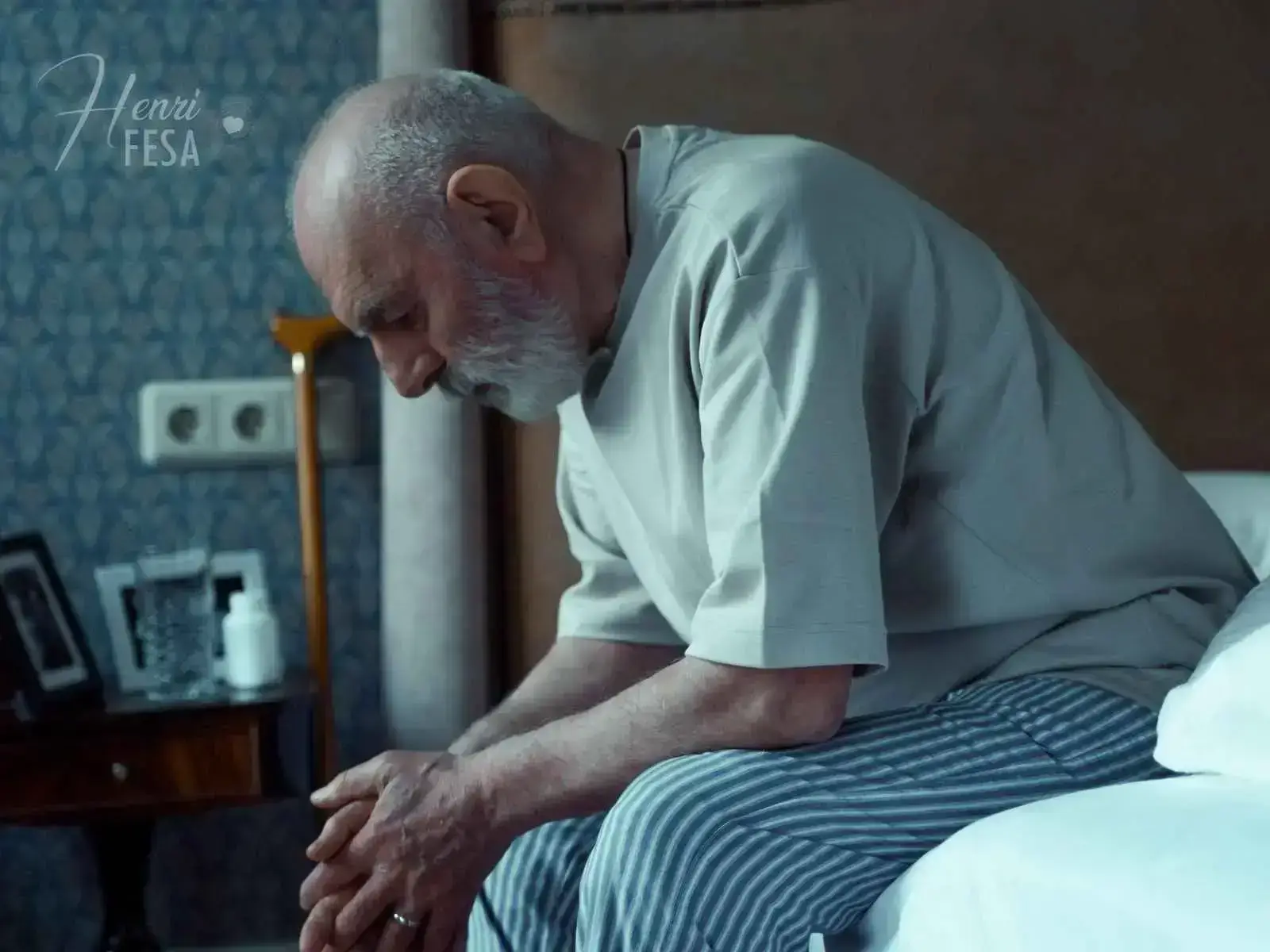 Homem 50+ sentado à beira da cama, cabisbaixo, com pensamentos negativos e tristezas, um dos motivos para o marido negativo existir!