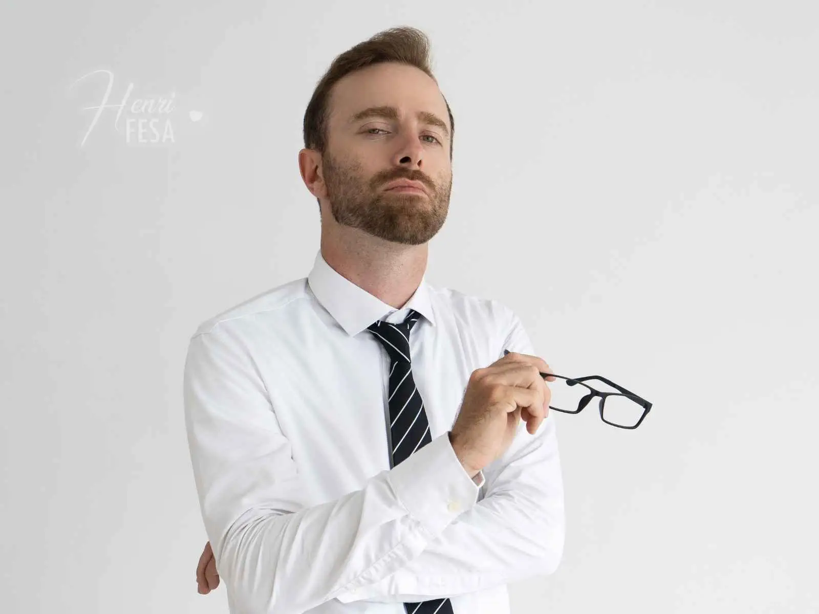 Homem de camisa social e gravata, segurando um óculos e olhando para baixo com um olhar arrogante, semelhante a um marido arrogante!