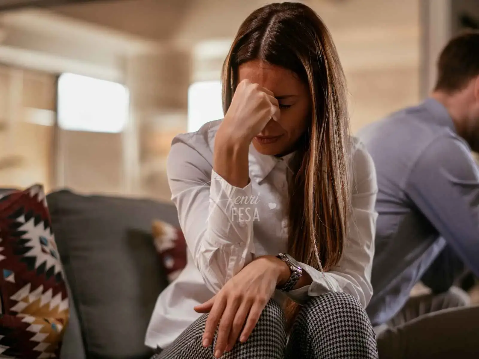 Mulher sentada à beira do sofá, com a mãos na testa como alguém que está refletindo, ao perceber que vive em um relacionamento rebote, e o homem logo atrás dela também sentado!