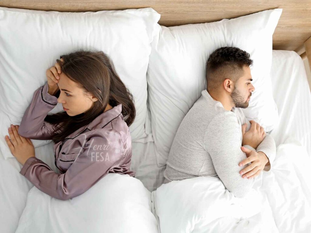 Sintomas de baixa libido feminina afetando o casamento! Mulher e homem deitados na cama, ambos de costas um para o outro com semblante de preocupação, pois ela sofre com os sintomas de baixa libido feminina e seu marido não entende!