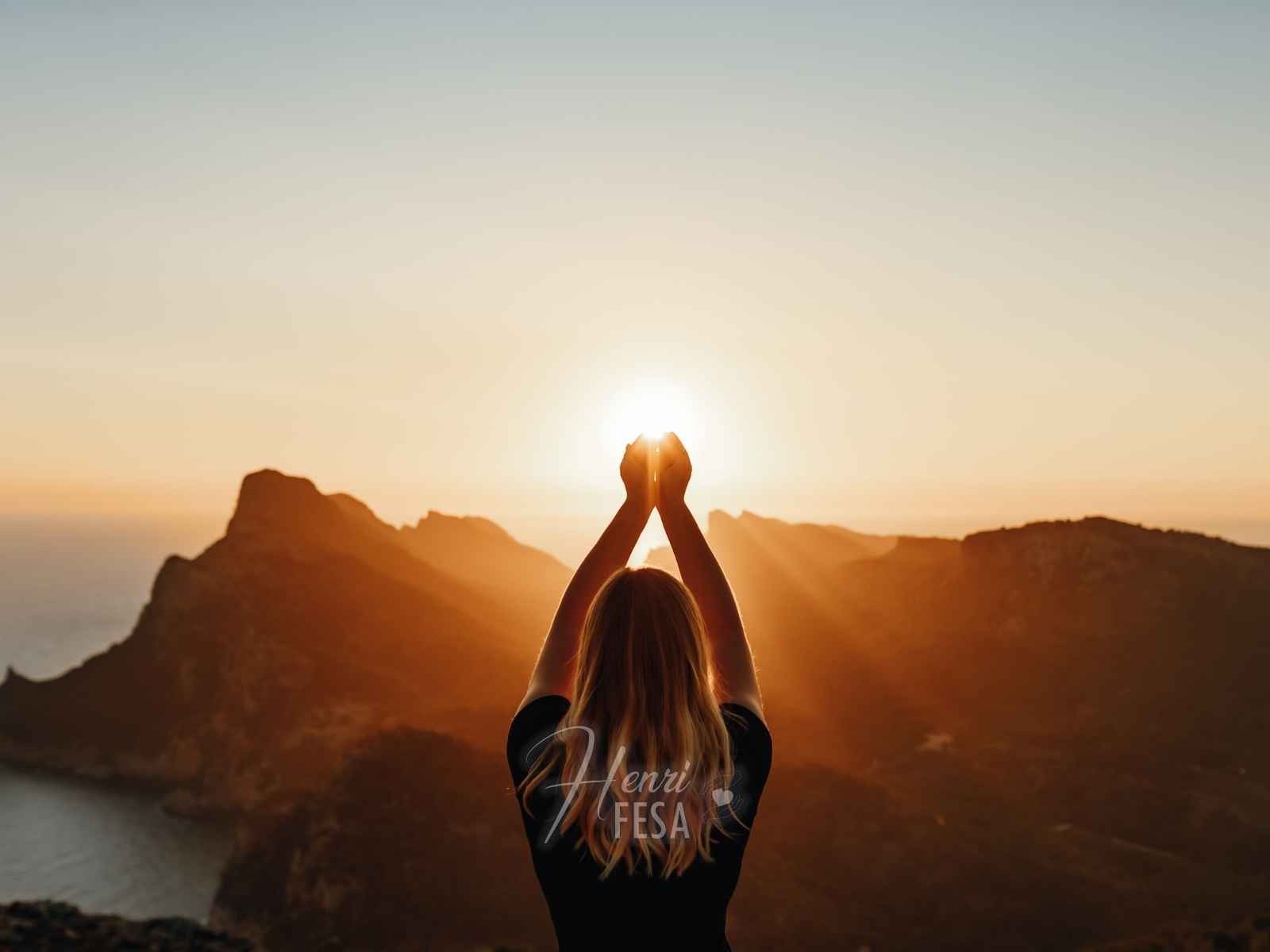Uma pessoa em frente a uma montanha com os braços e mãos apontando para o céu diante de um lindo por do sol, mostrando o que são Trabalhos Espirituais em andamento!